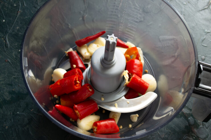 First Blending Stage Chunks of hot pepper and peeled garlic cloves inside a food processor bowl.