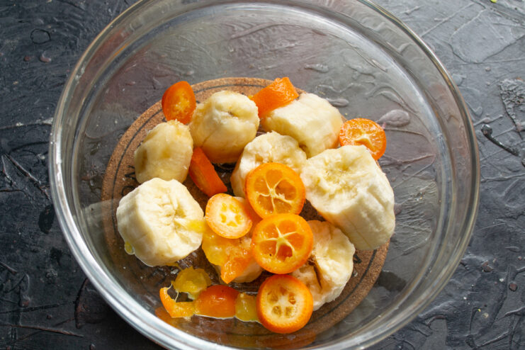 Preparing the fruit base Pieces of ripe banana and sliced kumquats in a glass mixing bowl