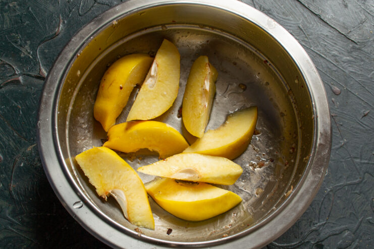 Prepping The Fruit Quince slices tossed with olive oil in a metal bowl