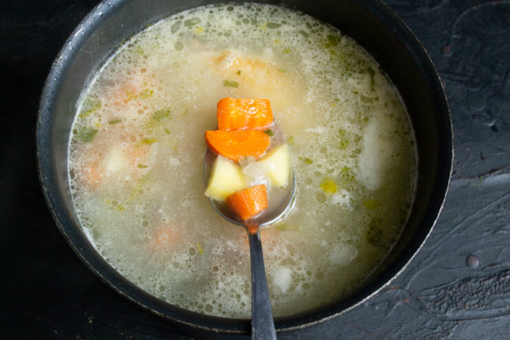 Adding Vegetables Spoon holding potato and carrot chunks in chicken broth