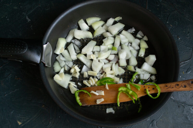 Adding minced garlic and chopped hot pepper to the sautéed onions in a skillet