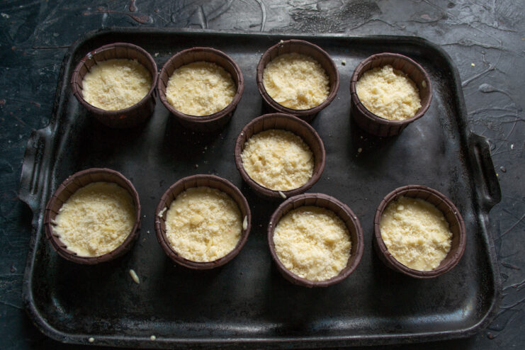 Adding the almond crumb topping Muffin batter in liners sprinkled with a buttery almond crumb topping