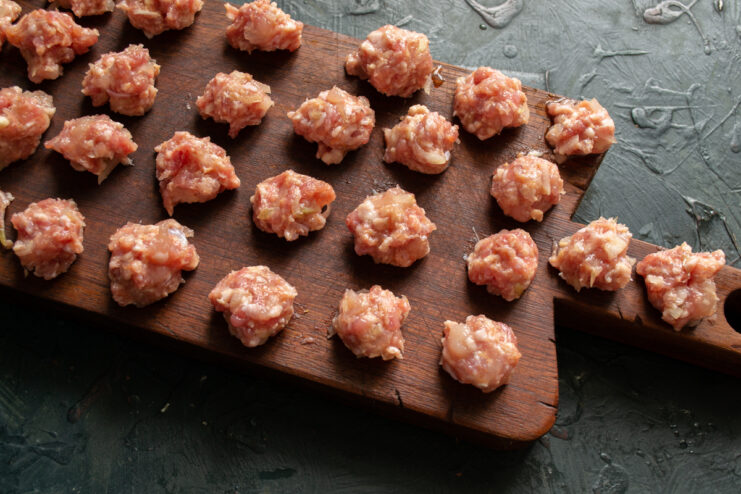 Shaping the meatballs Small raw meatballs placed on a wooden cutting board