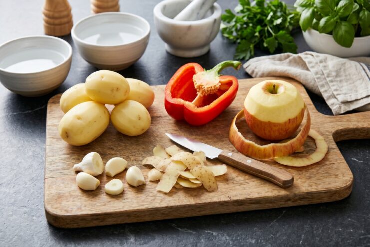 Small steel paring knife resting next to peeled apples and potatoes