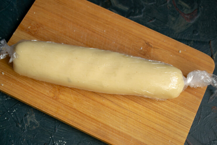 Smooth marzipan dough rolled into a log and wrapped tightly in plastic wrap