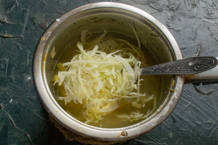 Stirring In the Cabbage Finely shredded cabbage inside a pot with simmering broth.