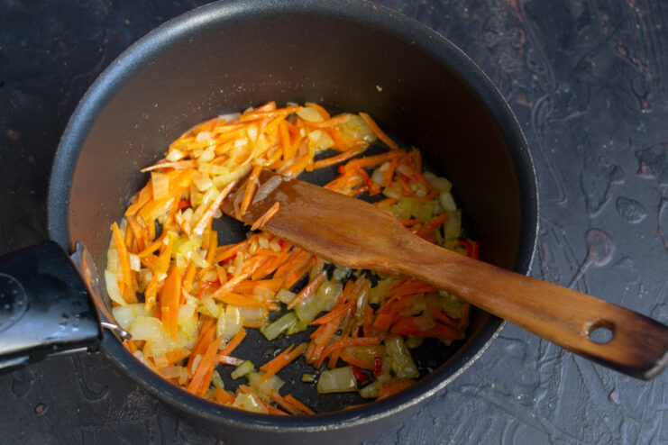 Adding Carrots To The Soup Julienned carrots added to sautéed onions and garlic in a pot.