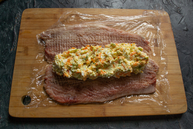 Filling spread down the center of pounded herring fillets on plastic wrap.