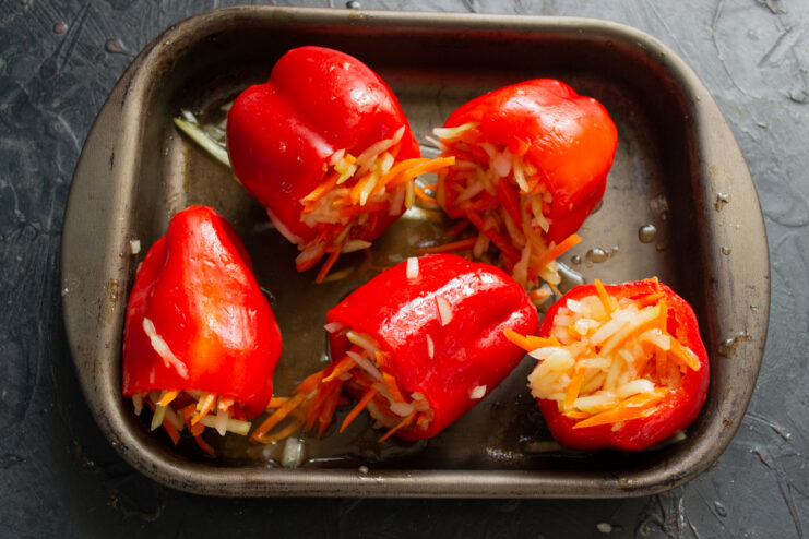 Stuffing the bell peppers Red bell peppers tightly stuffed with mixed vegetables on a baking sheet