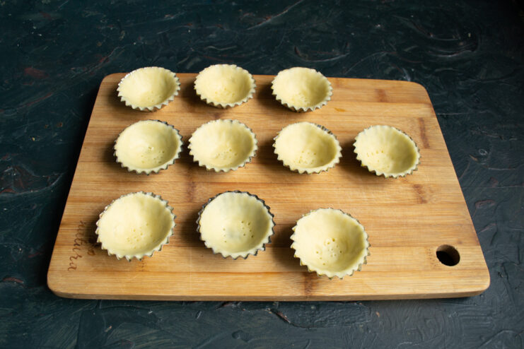 Pricking the tartlet bottoms with a fork Pricking the shortcrust pastry in the molds with a fork on a wooden board