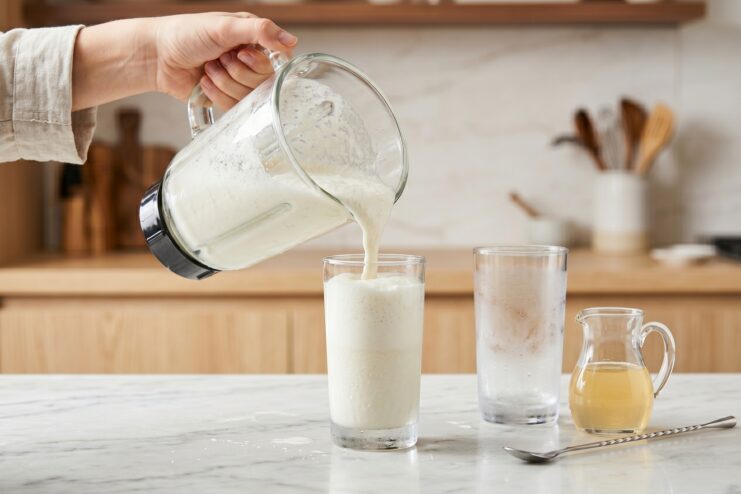 Pouring the Finished Milkshake A thick, freshly blended milkshake being poured from a blender pitcher into a tall glass.