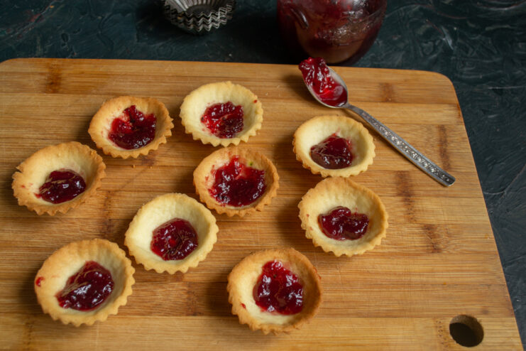 Adding a layer of sweet and sour jam Filling the shortcrust tartlets with a layer of berry jam
