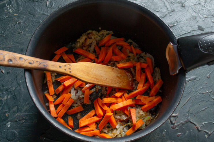Adding the carrots Sliced carrots joining the sautéed onions in a pot
