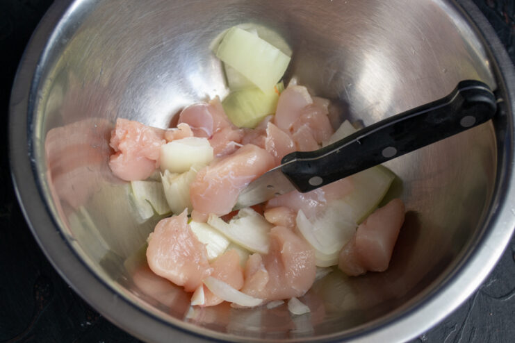 Preparing The Meatball Base Chunks of raw chicken breast and diced onion in a bowl.