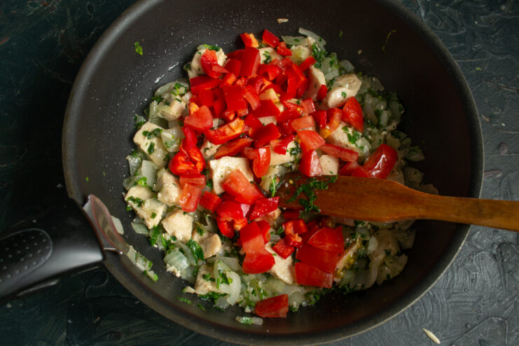 Adding diced bell peppers and tomatoes to the chicken in the pan