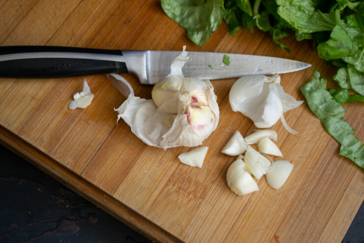 Prepping the Garlic Sliced young garlic cloves on a wooden cutting board