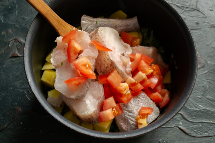 Adding the tomatoes Diced red tomatoes layered over fresh fish and vegetables in a pot