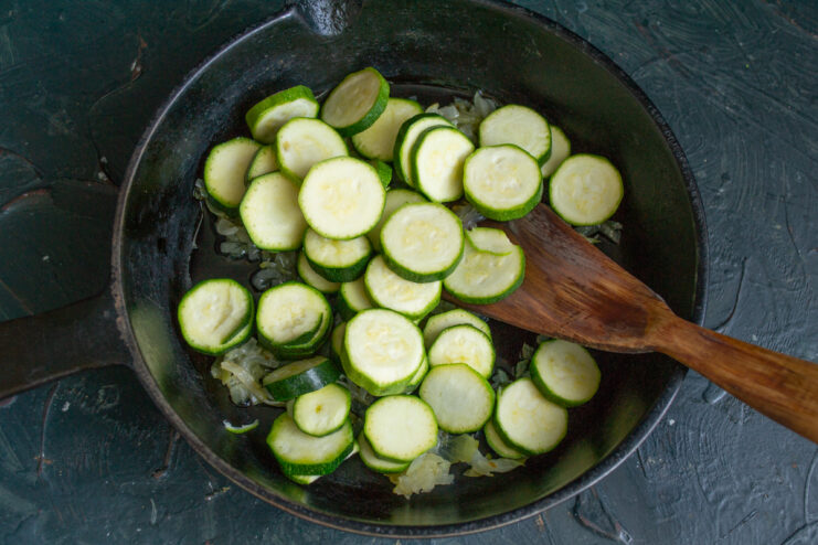 Adding the Zucchini Sliced young zucchini rounds added to sautéed onions in a skillet