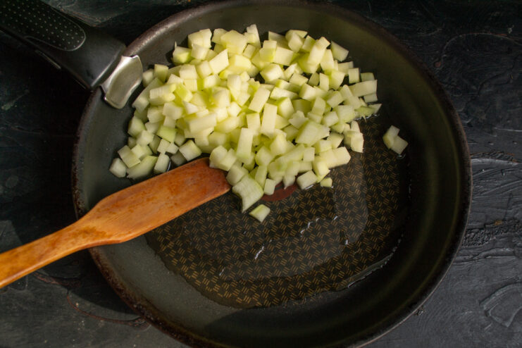Diced zucchini cooking in a skillet with olive oil.