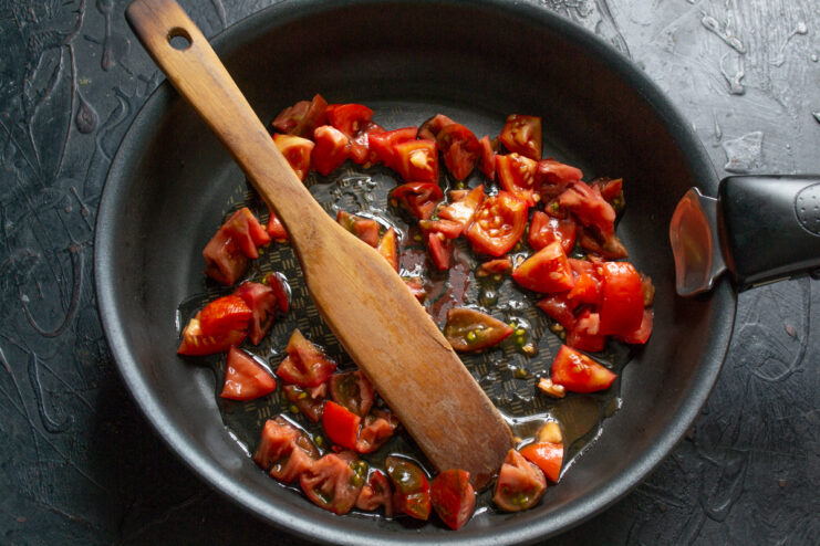 Diced red tomatoes cooking in a skillet with oil