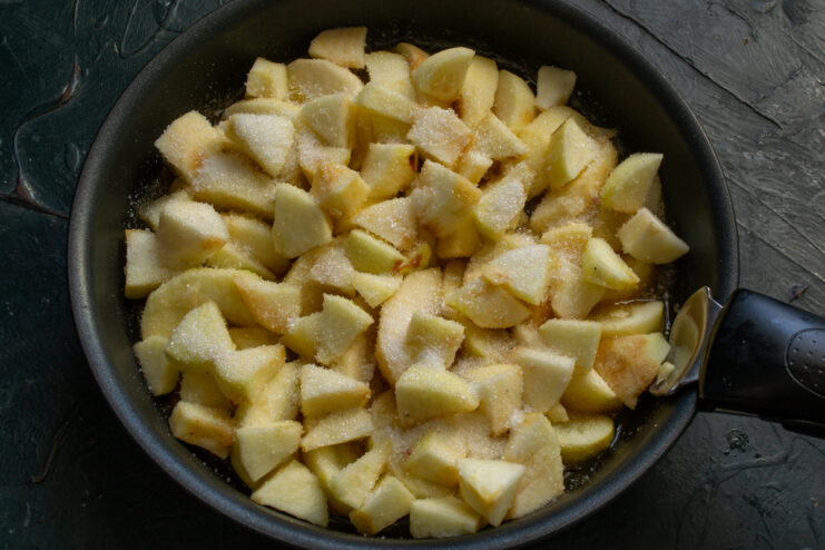 Diced apples covered in sugar placed over the sliced apples in a skillet.