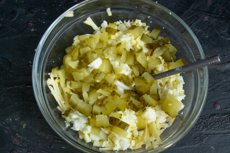 Adding pickles Chopped pickles in a bowl with eggs and grated apple.