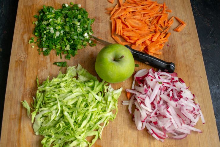 Sliced vegetables including cabbage, radishes, carrots, and scallions on a board