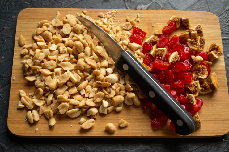 Chopping the nuts and dried fruits Chopped peanuts, figs, and dried cherries on a wooden cutting board