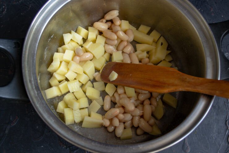 Vegetable base for the soup Diced potatoes and whole white beans at the bottom of a soup pot