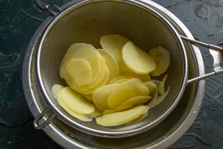 Rinsing the potatoes Thinly sliced potatoes draining in a metal sieve
