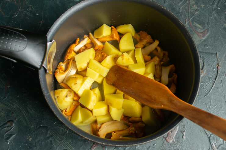 Adding the potatoes Large diced potatoes in a pan with sautéed chanterelle mushrooms