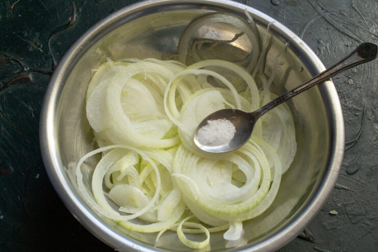 Preparing onions for fritters Thinly sliced onion rings sprinkled with salt in a metal bowl.