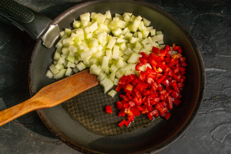 Diced red bell pepper added to zucchini in a skillet.
