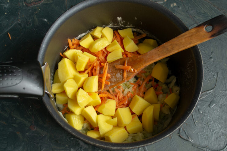 Adding potatoes Dropping diced potatoes into the pot with sauteed vegetables