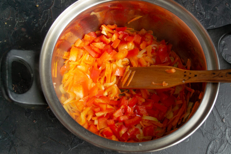 Adding sweet bell pepper Diced sweet red bell pepper mixed with vegetables in a pot