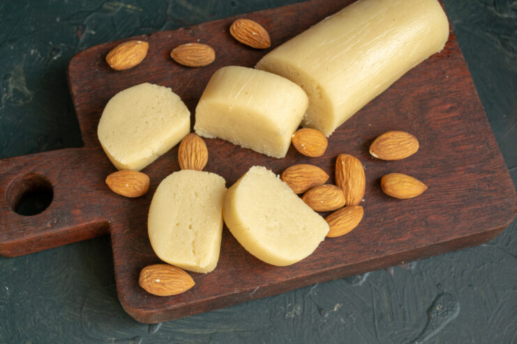 Slices of fresh homemade marzipan resting on a dark wooden cutting board