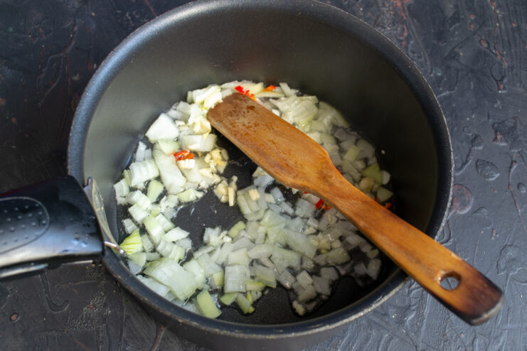 Sautéing The Soup Base Chopped onions, garlic, and chili sautéing in a pot with oil.