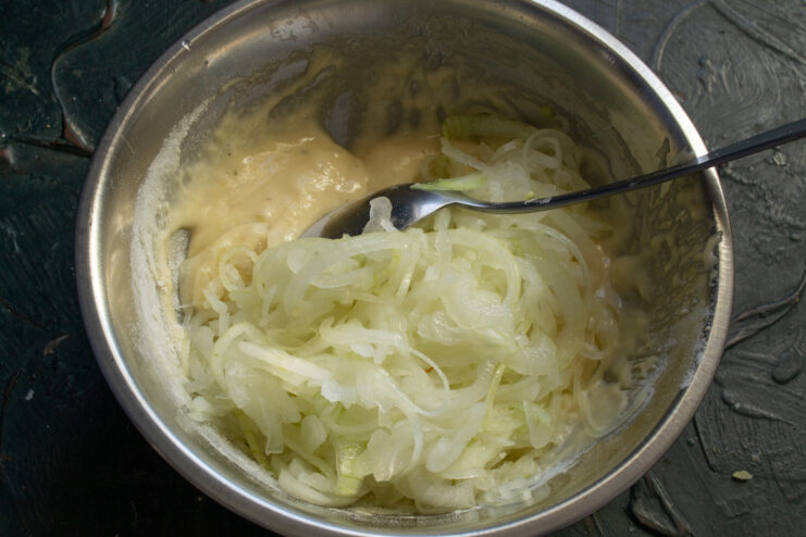 Combining onions with batter Sliced onions being added to a bowl with thick batter.