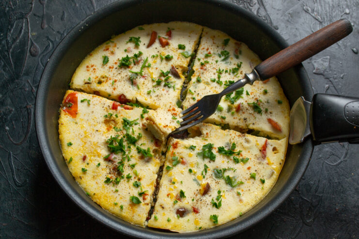 Sliced vegetable omelet in a skillet with a fork and fresh herbs