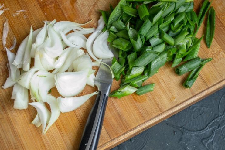 Slicing Onions for the Salad Sliced yellow onion wedges and chopped green onions on a cutting board