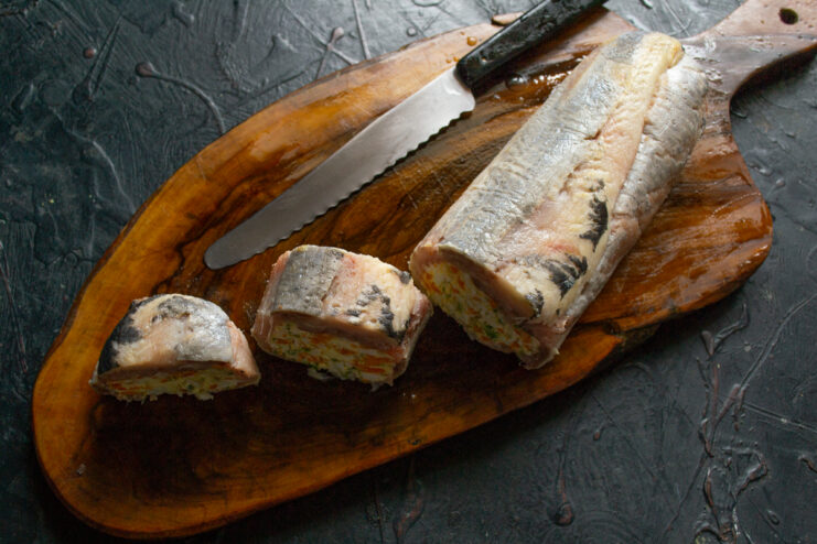 Slicing the finished chilled herring roll with a knife on a wooden board.