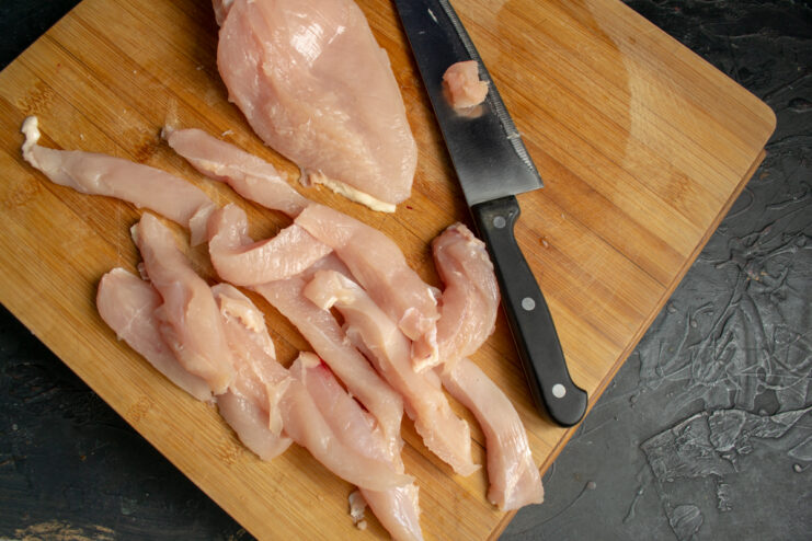 Slicing the chicken fillet Slicing raw chicken fillet into thick strips on a wooden board
