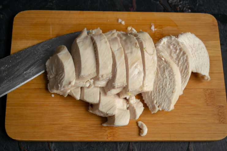 Dicing the cooked chicken Cutting cooked chicken breast into small cubes on a cutting board
