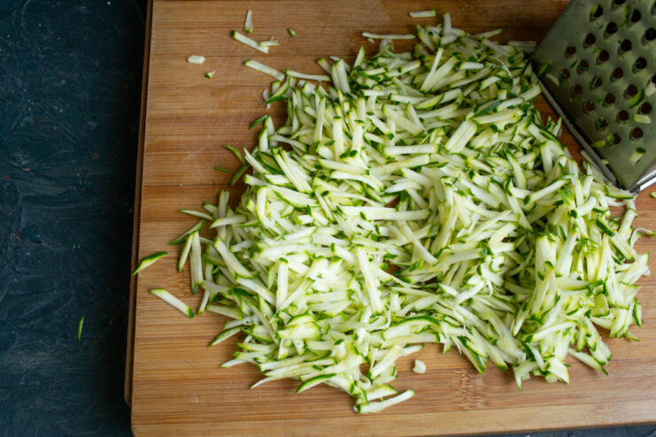 Preparing the zucchini Freshly grated zucchini on a wooden cutting board.
