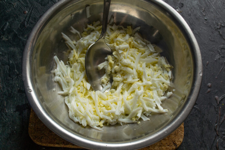 Coarsely grated hard-boiled eggs in a metal mixing bowl.