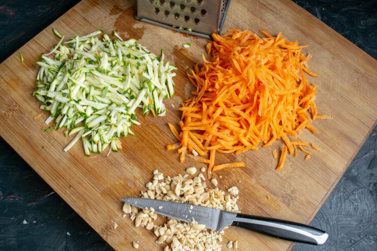 Grated carrots, shredded zucchini, and chopped peanuts on a board