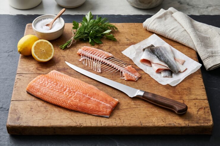 Flexible boning knife positioned near a fresh salmon fillet and fish bones