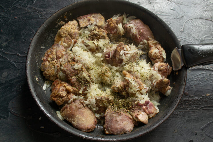 Adding herbs to the liver Seared chicken liver mixed with sautéed onions and herbs in a skillet.