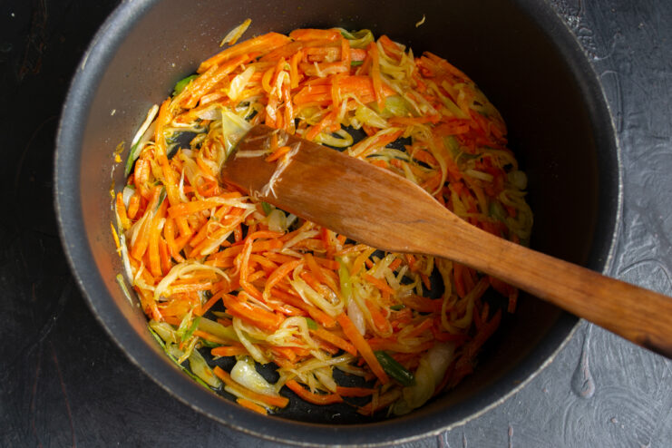 Sautéing The Vegetables Root vegetables sautéed to softness in a pot stirred with a wooden spatula.