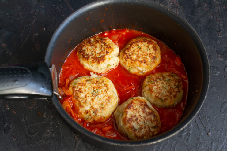 Meatballs In Tomato Sauce Browned chicken meatballs resting on top of a tomato and vegetable base in a pot.
